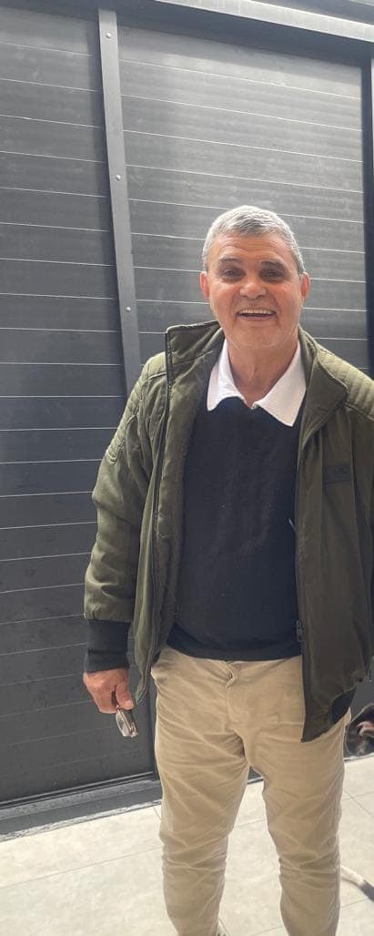 Carlos Oliveira, de jaqueta verde, sorrindo.