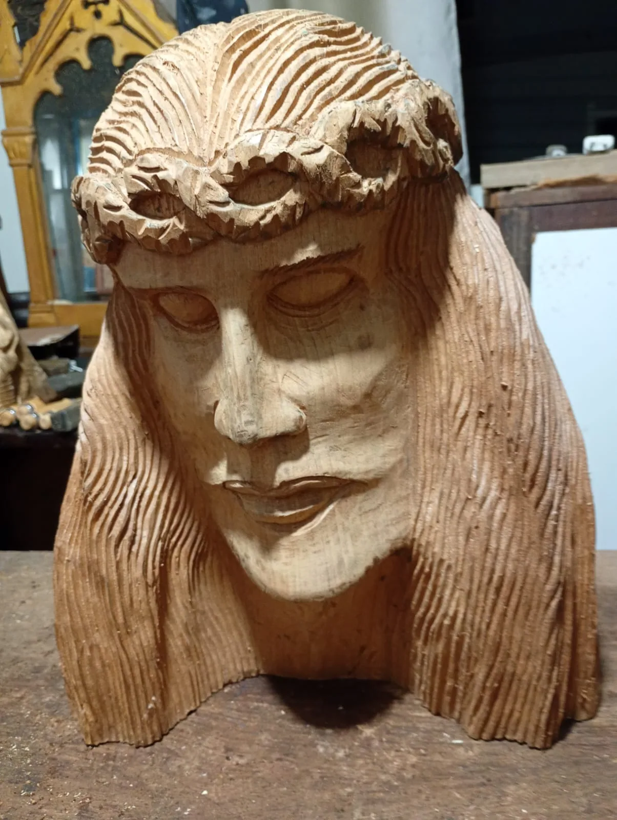 Busto de Cristo com coroa de espinhos, entalhado em madeira por Carlos Oliveira, na bancada da oficina.